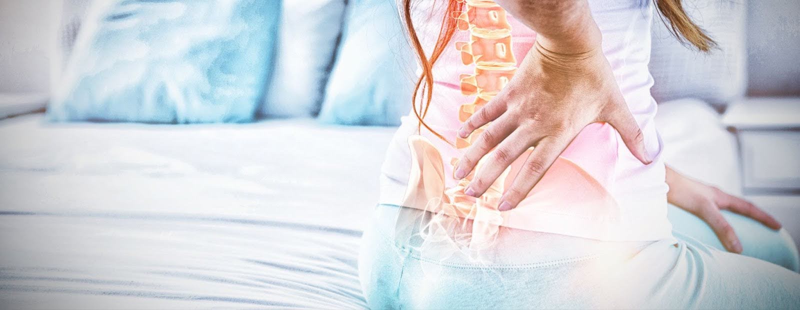 Woman sitting on bed holding lower back to illustrate spinal pain.