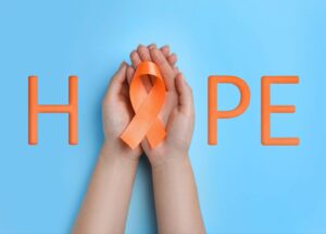 Person holding orange CRPS ribbon in hands with letters overlaid that spell out the word hope.