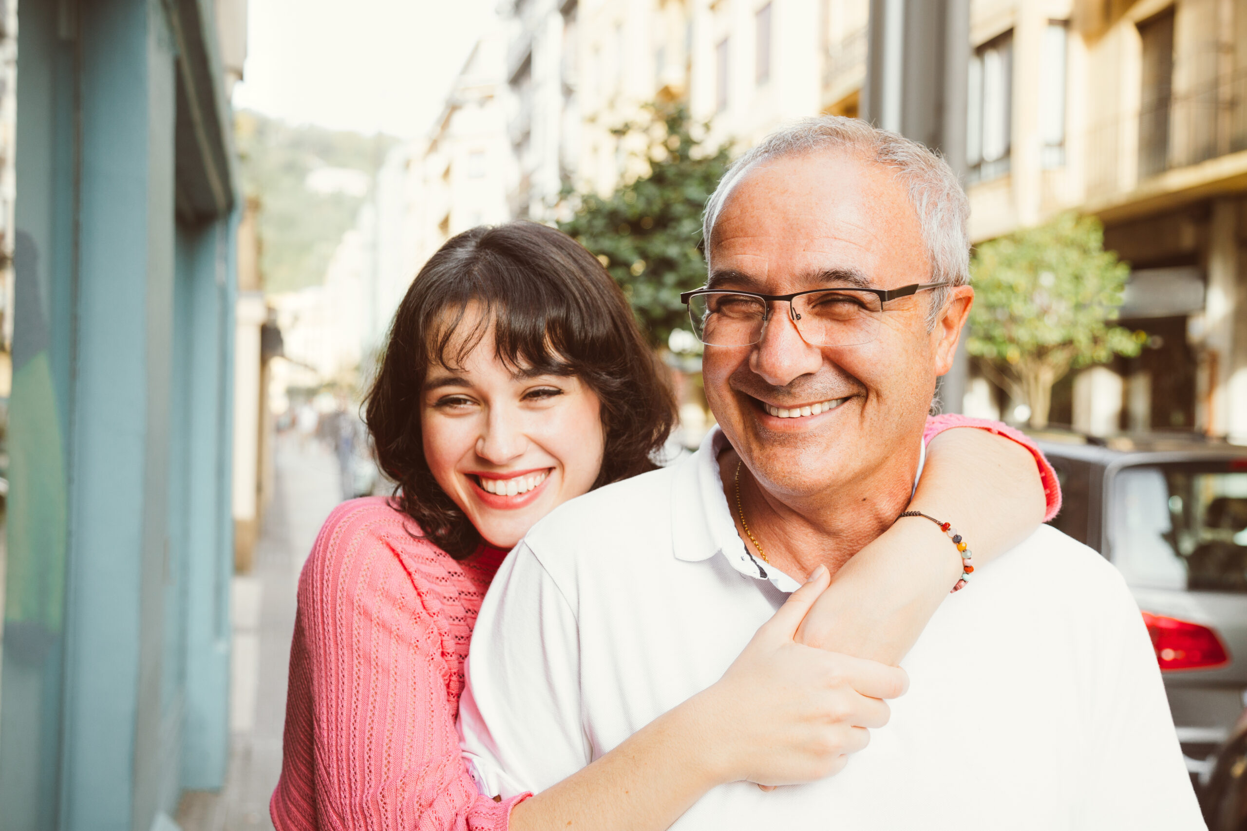 Middle-aged father and adult daughter embracing in the street.